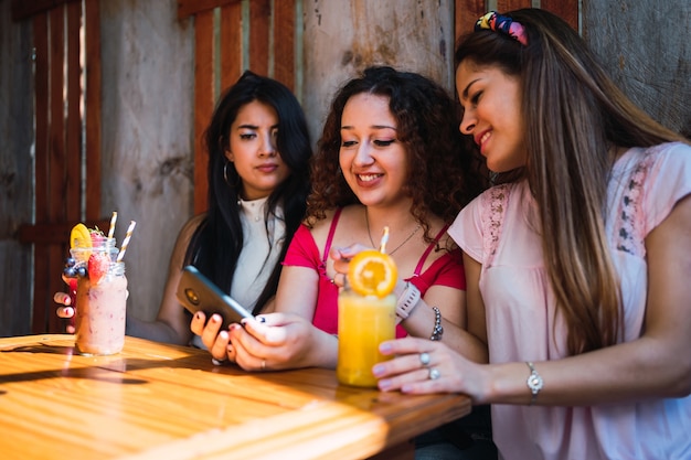 Un groupe d'amis buvant un jus de fruits ensemble et regardant le smartphone.