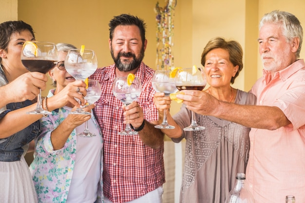 groupe d'amis caucasiens d'âges différents célèbrent ensemble en applaudissant avec des cocktails tous ensemble s'amusant