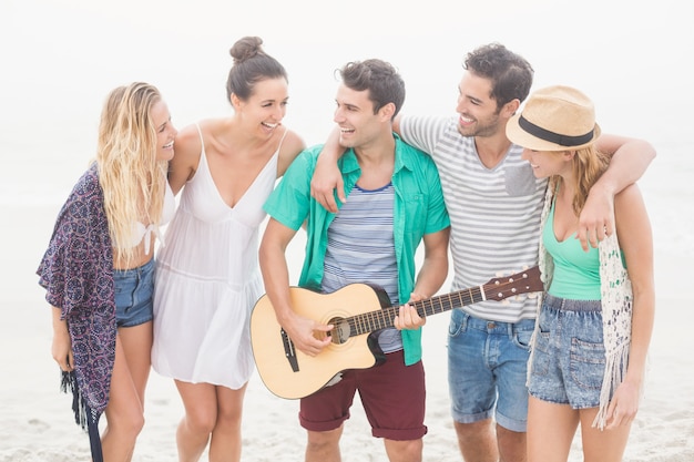 Groupe d'amis debout sur la plage avec une guitare