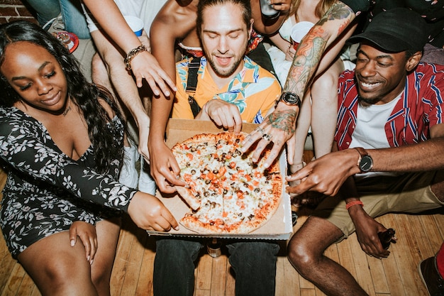 Photo groupe d'amis divers dégustant une pizza lors d'une fête