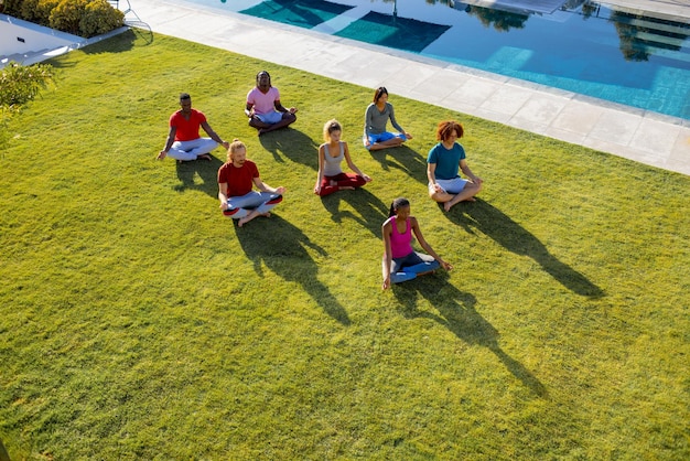 Groupe d'amis divers faisant du yoga et méditant dans le jardin. Amitié, mode de vie sain et actif, été, soleil, inchangé.