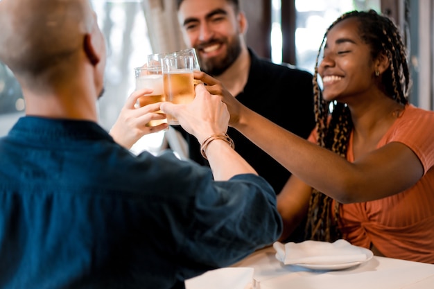 Groupe d'amis divers portant un toast avec des verres à bière tout en savourant un repas ensemble dans un restaurant. Notion d'amis.