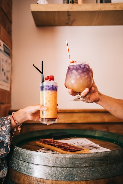 Un groupe d'amis est assis sur la terrasse en été derrière un tonneau en bois avec des cocktails et une collation