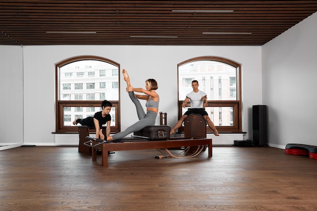 Groupe d'amis faisant des exercices de pilates fessiers agenouillés sur des lits réformateurs dans une salle de sport dans un concept de santé et de remise en forme