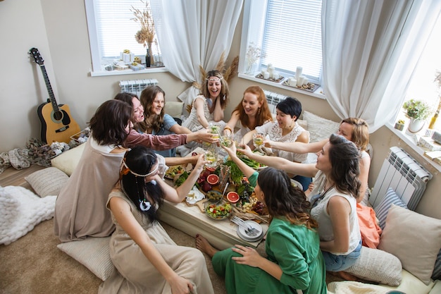 Groupe d'amis féminins hippie moderne célébrant des vacances à table servant avec des aliments sains