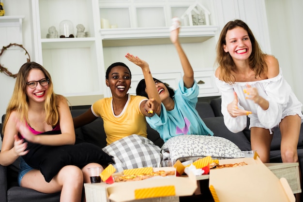 Un groupe d&#39;amis de femme divers assis sur le canapé en train de manger une pizza ensemble