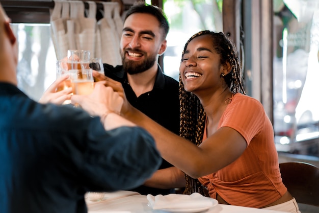 Groupe d'amis grillant avec des verres à bière dans un restaurant.