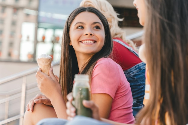 Un groupe d'amis heureux d'adolescents multiraciaux mangeant une délicieuse crème glacée en train de parler assis dans la rue