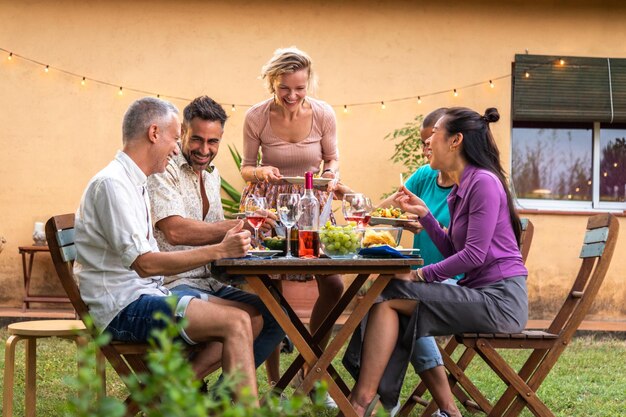 Un groupe d'amis heureux assis à table, mangeant, riant, s'amusant, mangeant et buvant du vin.