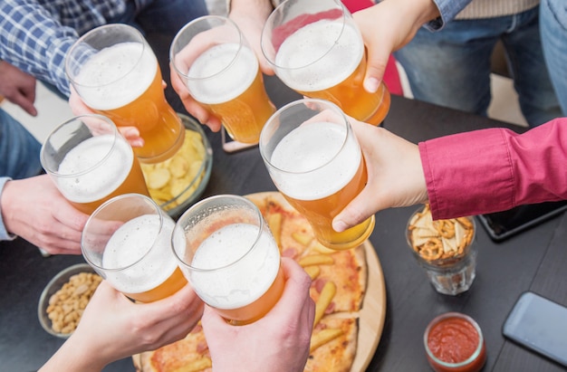 Groupe d'amis heureux boire et griller de la bière au pub