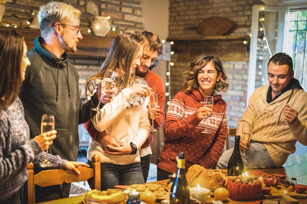 Groupe D'amis Heureux Célébrant La Fête De Noël Avec Du Vin Blanc Et Des Mets Sucrés Au Dîner