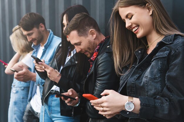 Groupe d'amis jeunes et élégants utilisant des smartphones pour la messagerie au lieu d'une véritable communication