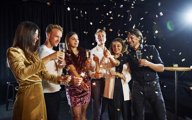 Groupe d'amis joyeux célébrant le nouvel an à l'intérieur avec des boissons à la main.