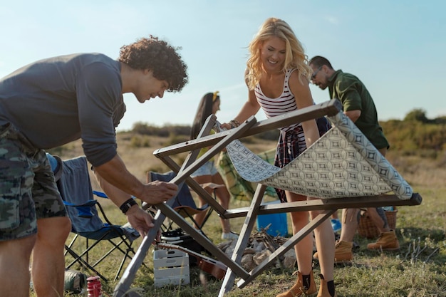 Un groupe d'amis joyeux se préparant au camping et installant une chaise de repos sur un endroit approprié en été.