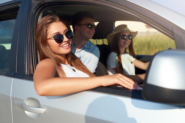 Un groupe d'amis a loué une voiture lors d'un voyage d'été et est arrivé à la plage de la mer. Une femme à lunettes regarde par la fenêtre de la voiture.