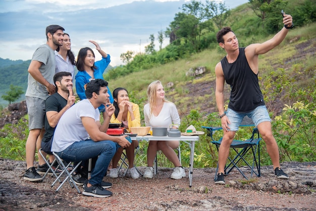 Un groupe d'amis masculins et féminins prépare une table de pique-nique au milieu de belles montagnes et selfie