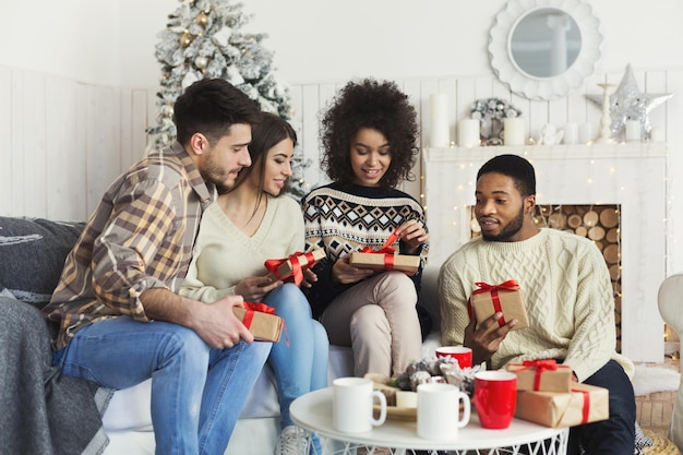 Groupe d'amis multiethniques heureux échangeant des cadeaux de Noël à la maison, espace de copie