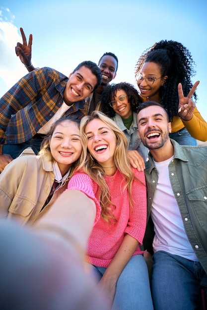 Un groupe d'amis multiethniques prenant un selfie avec un téléphone portable intelligent à l'extérieur