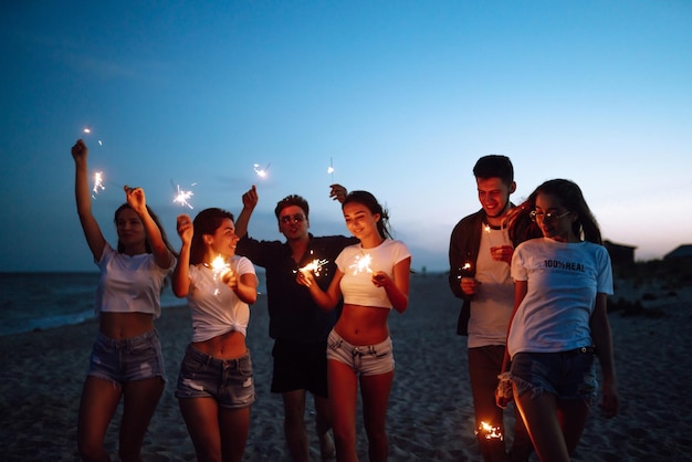 Groupe d'amis la nuit sur la plage avec des cierges magiques Jeunes amis profitant de vacances à la plage