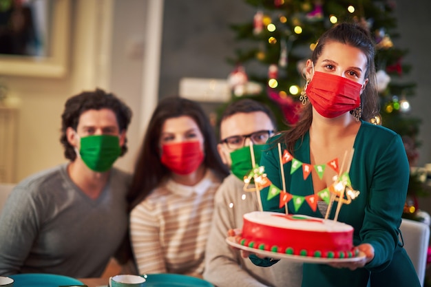groupe d'amis portant des masques de protection tout en célébrant Noël à la maison en dégustant un gâteau de Noël