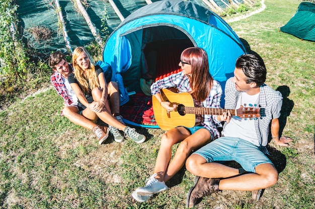 Groupe d'amis s'amusant à chanter en plein air au camp de pique-nique avec guitare vintage