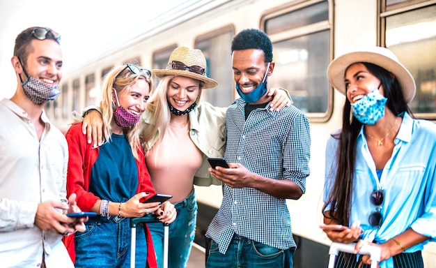 Groupe d'amis s'amusant avec les téléphones intelligents mobiles en attendant le train à la gare