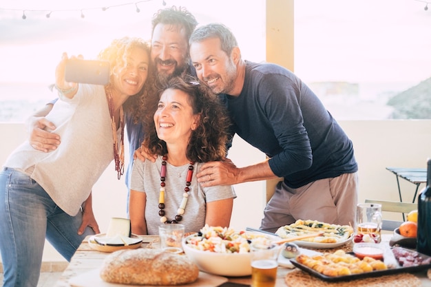 Un groupe d'amis s'amuse ensemble lors d'un déjeuner en plein air sur la terrasse à la maison et prend un selfie moderne avec un téléphone intelligent à partager sur les comptes de médias sociaux pour la vie sur Internet