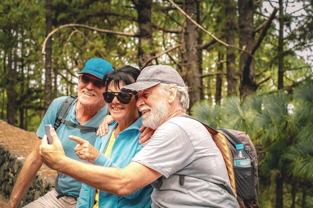 Groupe d'amis seniors heureux en excursion en montagne regardant le téléphone en riant assis pour se reposer