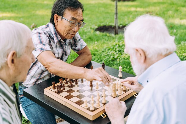 Groupe d'amis seniors jouant aux échecs dans le parc. Concepts de style de vie sur l'ancienneté et le troisième âge