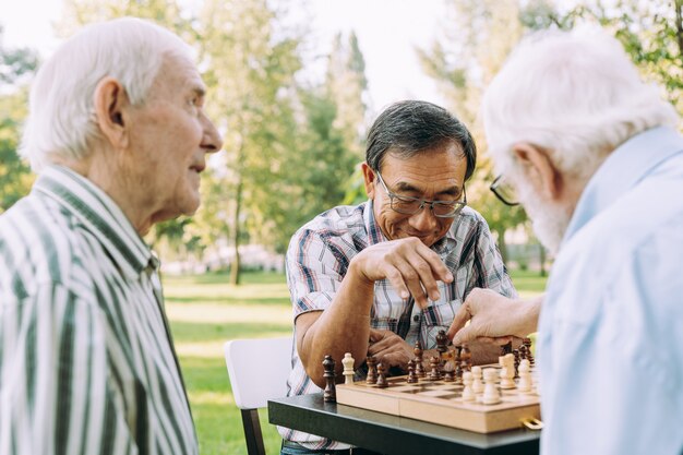 Groupe d'amis seniors jouant aux échecs dans le parc. Concepts de style de vie sur l'ancienneté et le troisième âge