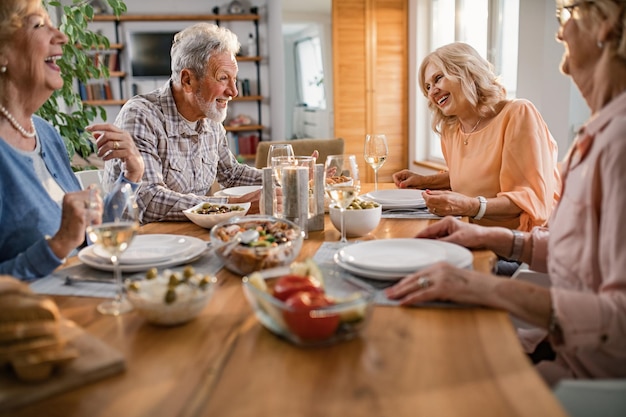 Groupe d'amis seniors s'amusant tout en parlant pendant le déjeuner à la table à manger