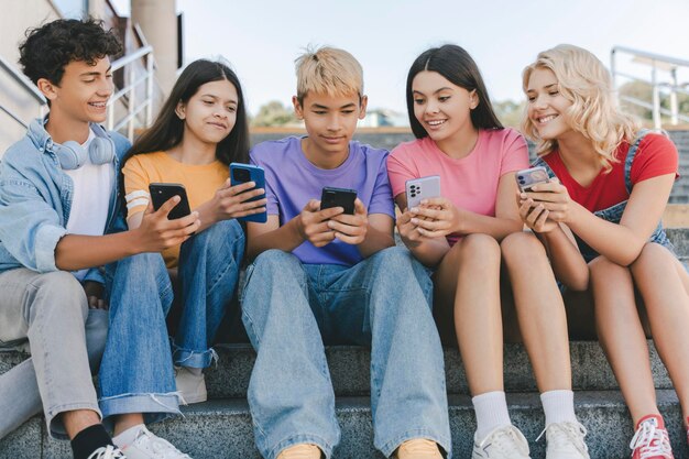 Photo groupe d'amis souriants adolescents tenant des téléphones portables regardant la communication vidéo en ligne