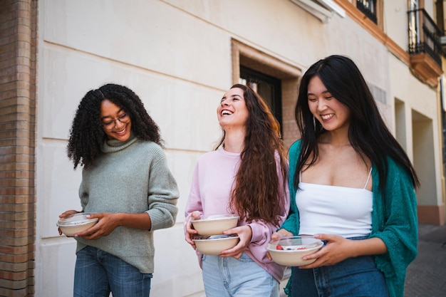 Photo un groupe d'amis souriants ramassent de la nourriture dans des bols ils marchent dans la rue