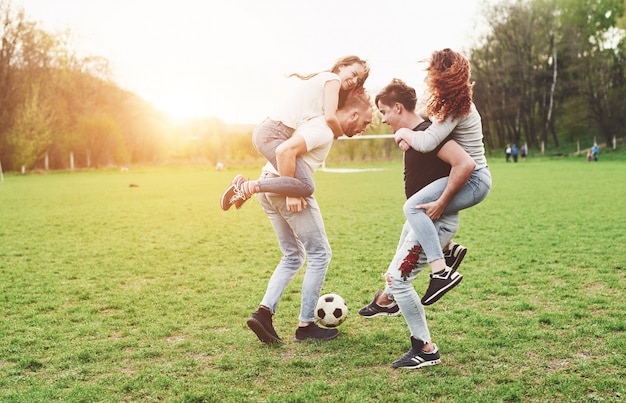 Un groupe d'amis en tenue décontractée joue au soccer en plein air. Les gens s'amusent et s'amusent. Repos actif et coucher de soleil pittoresque.