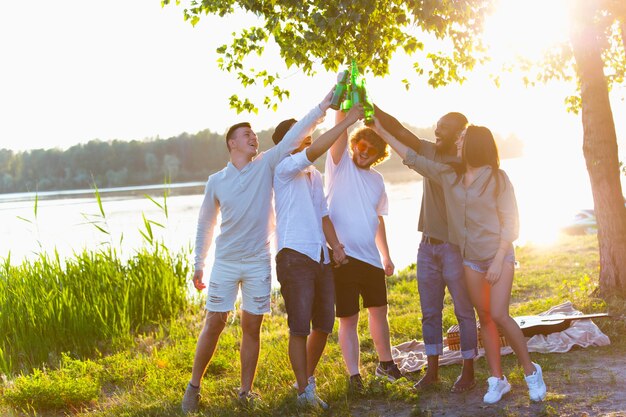 Groupe d'amis tintant des bouteilles de bière pendant le pique-nique à la plage.