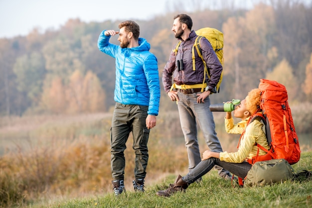 Groupe d'amis en vestes colorées faisant une pause avec des sacs à dos à l'extérieur sur la pelouse verte