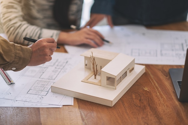 Groupe d'un architecte travaillant et discutant d'un modèle d'architecture avec du papier à dessin d'atelier sur une table au bureau