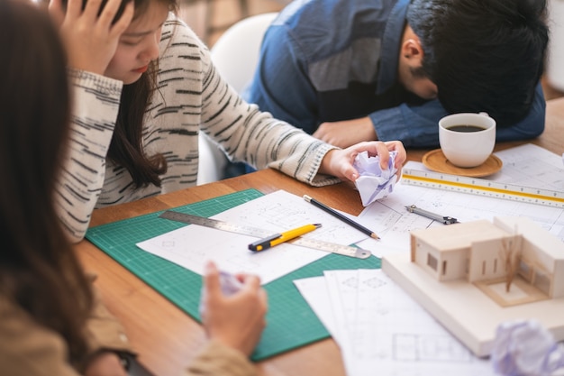 Un groupe d'architectes se sent stressé après avoir travaillé sur un modèle d'architecture avec du papier à dessin d'atelier sur une table au bureau