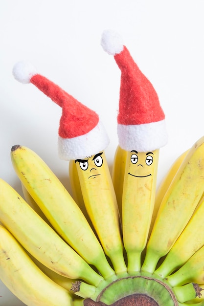 Groupe de bananes dans des chapeaux de noël jouets avec des émotions dessinées sur fond blanc