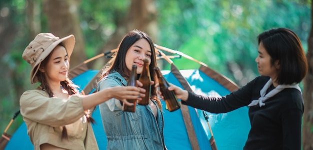 Groupe de belles femmes asiatiques amis voyageurs se détendant devant la tente de camping Ils aiment parler et boire de la bière avec plaisir et heureux ensemble