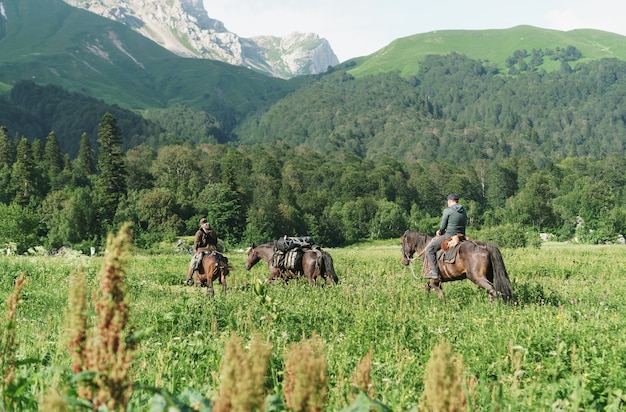 Un groupe de cavaliers à cheval sur le terrain dans le contexte des sommets des montagnes.