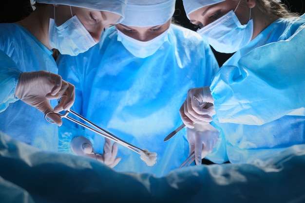 Groupe de chirurgiens au travail en salle d'opération aux tons bleus. Équipe médicale effectuant l'opération