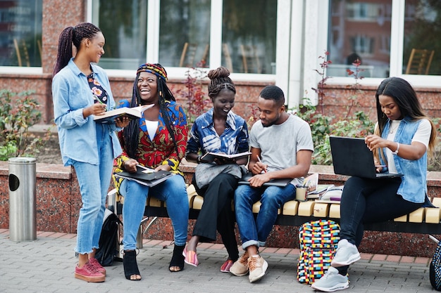 Photo groupe de cinq étudiants africains passant du temps ensemble sur le campus de la cour de l'université amis afro noirs étudiant sur un banc avec des articles scolaires ordinateurs portables cahiers