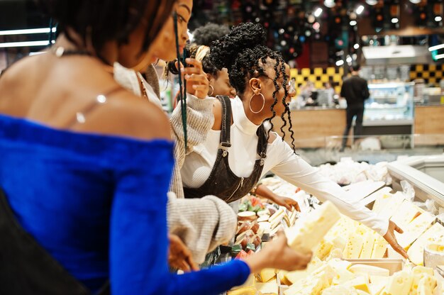 Groupe de cinq femmes avec des caddies choisissent le fromage dans un supermarché