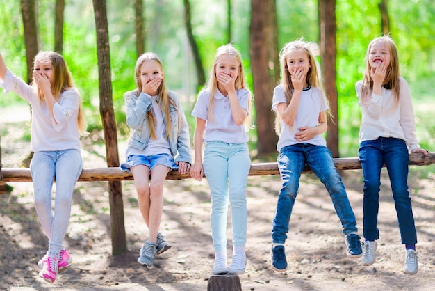 Un groupe de cinq filles drôles d'enfants lors d'une promenade dans la forêt d'été Asseyez-vous sur la poutre d'un arbre Journée ensoleillée