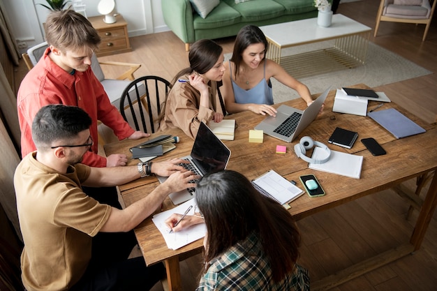 Groupe de cinq utilisant des ordinateurs portables et des cahiers pour apprendre lors d'une session d'étude