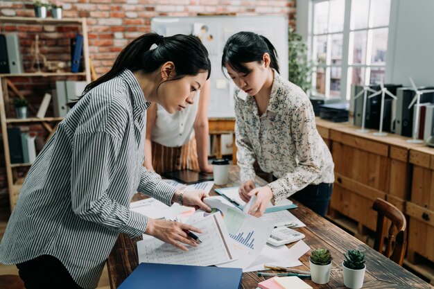 groupe de collègues dames trouvant une feuille de données lors d'une réunion d'entreprise dans un bureau moderne. collègues de jeunes filles debout à table dans la salle de conférence à la recherche de documents. concept d'entreprise de démarrage.