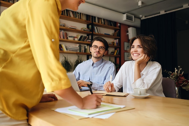 Groupe de collègues de travail souriants assis au bureau avec un ordinateur portable tout en parlant joyeusement au travail dans un bureau moderne