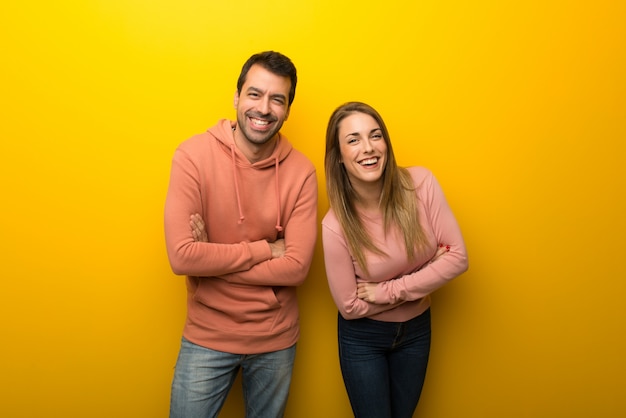 Groupe de deux personnes sur fond jaune, gardant les bras croisés en souriant