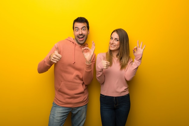 Groupe de deux personnes sur fond jaune montrant le signe ok